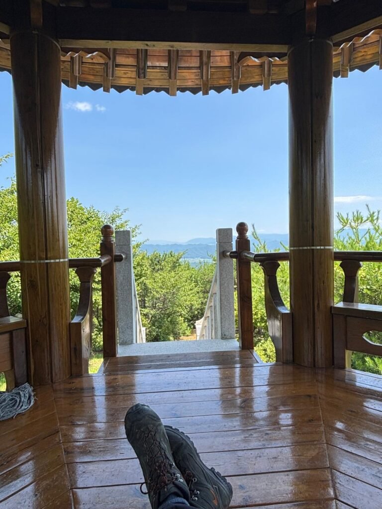 Sitting inside Cheonggeumjeong Pavilion with my feet in the frame, looking out at the green hills and mountains.