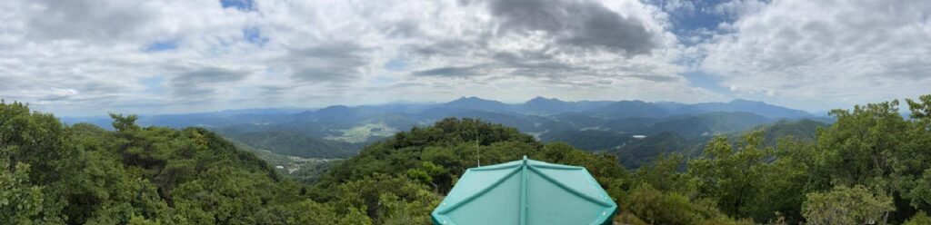 Panoramic view from the summit of Misungsan with the green hut and forested mountain landscape