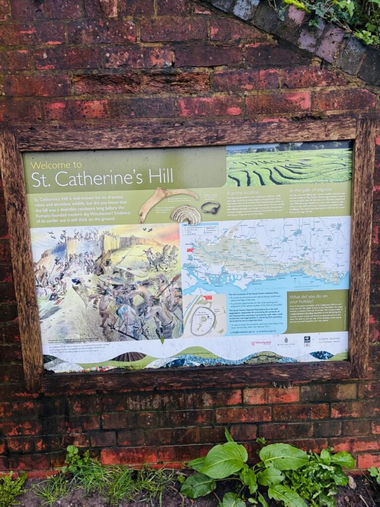 A sign with information and a map of St Catherine's Hill in Winchester. Mounted on a bridge wall