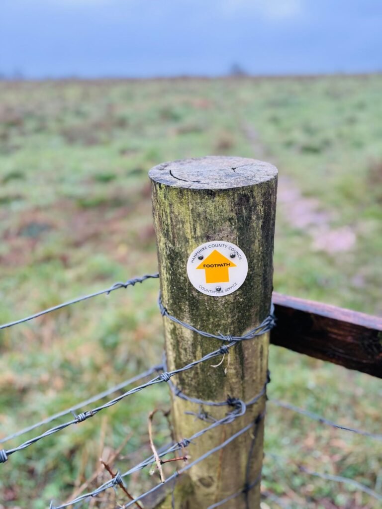 A Hampshire County Council footpath sign attached to a post by a gate close to St Catherine's Hill Winchester and the M3 motorway