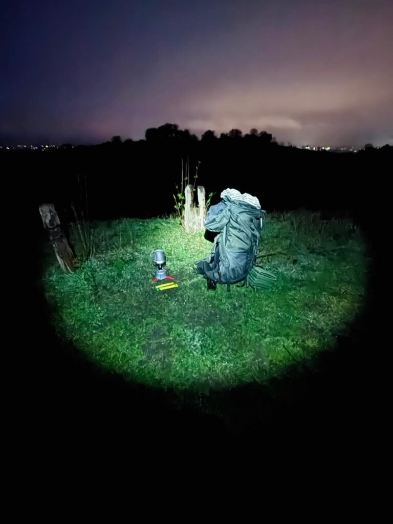 Head torch illuminating a grass area of an Osprey 48 litre backpack, Cooking stove with a SilverAnt titanium cup heating up water on the top for instant coffee