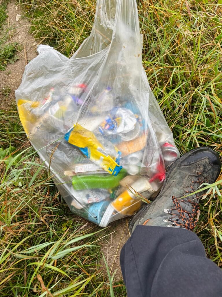 Bag of collected cans and bottles from a wild camping litter pick placed on the ground next to my Scarpa boot for scale