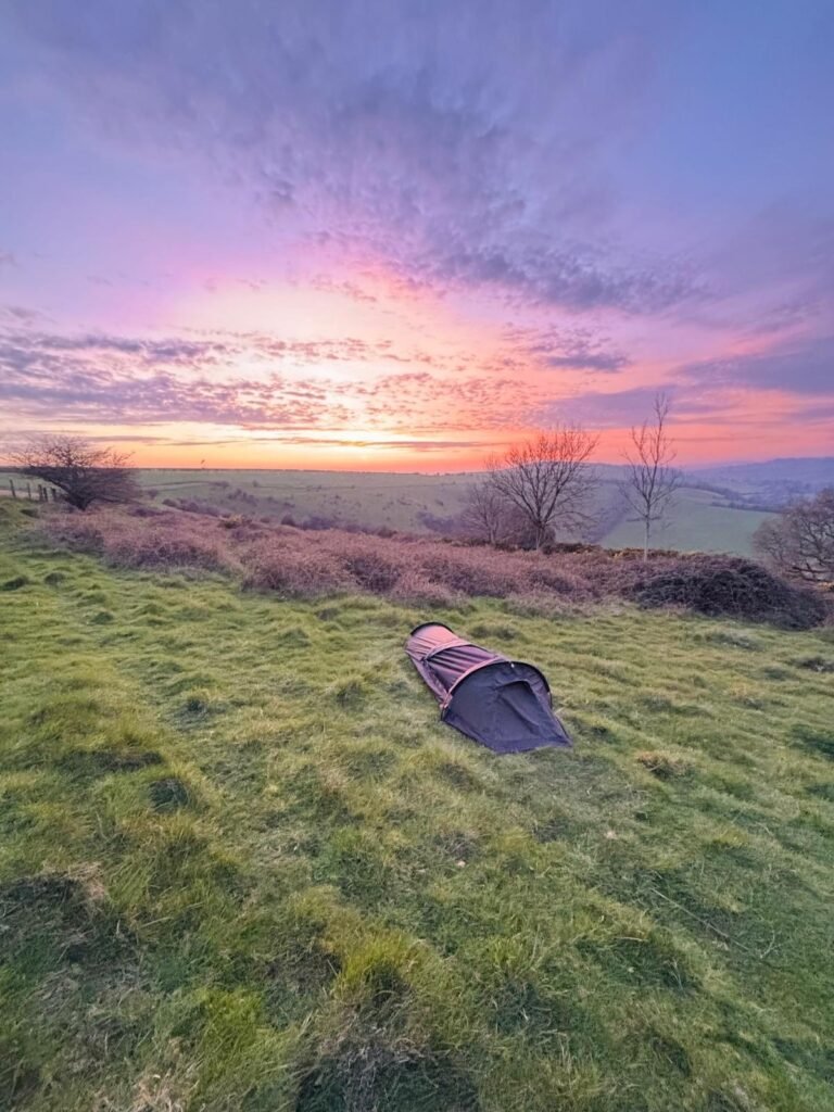The Nortent Skjul wild camping set up on a grass hill with a pink and red sunset on the horizon.