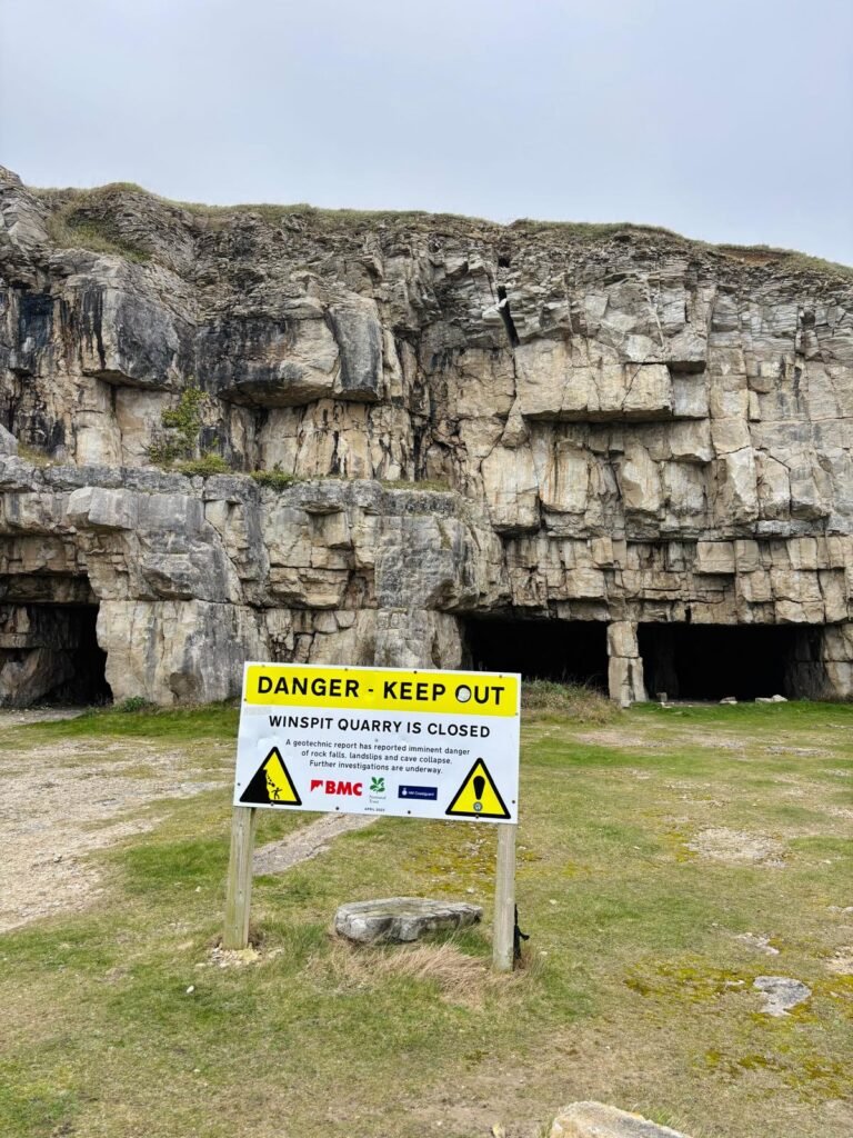 Rock walls and quarry entrance at Winspit Quarry with a large warning sign about safety hazards