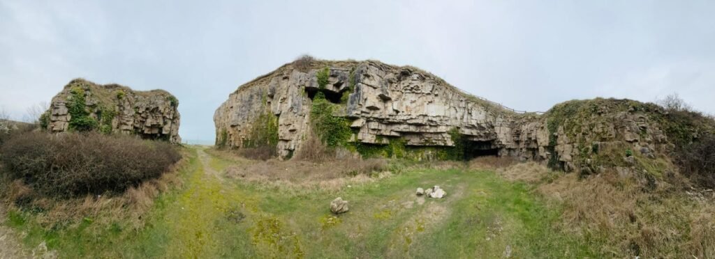 Panoramic view of Winspit Quarry with tall rock faces, flat grassy areas suitable for camping