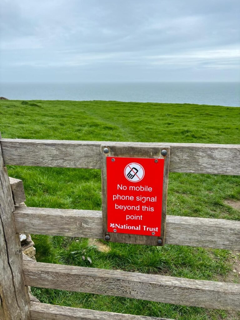Bright red National Trust warning sign on a gate at the top of high ground, stating no mobile phone signal beyond this point