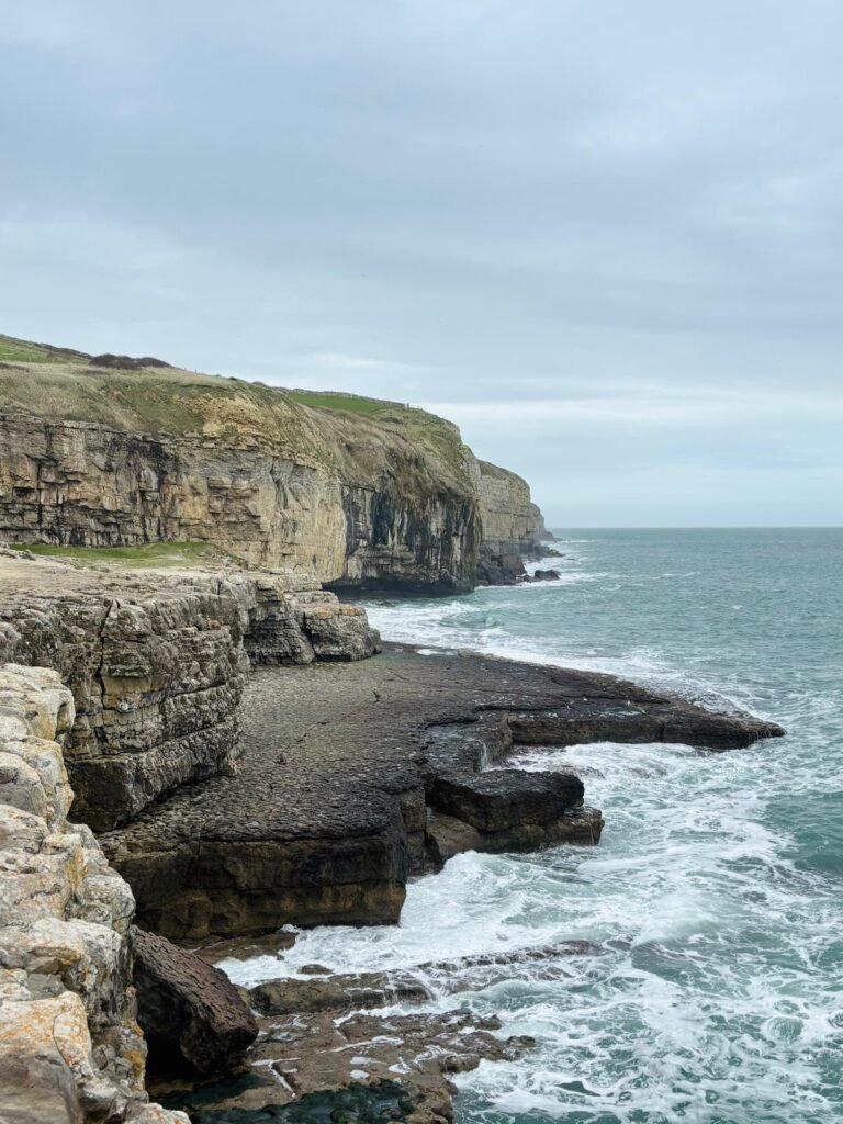 Rocky flat ledge at Dancing Ledge with the sea in front and high coastal cliffs rising behind on the Dorset coast