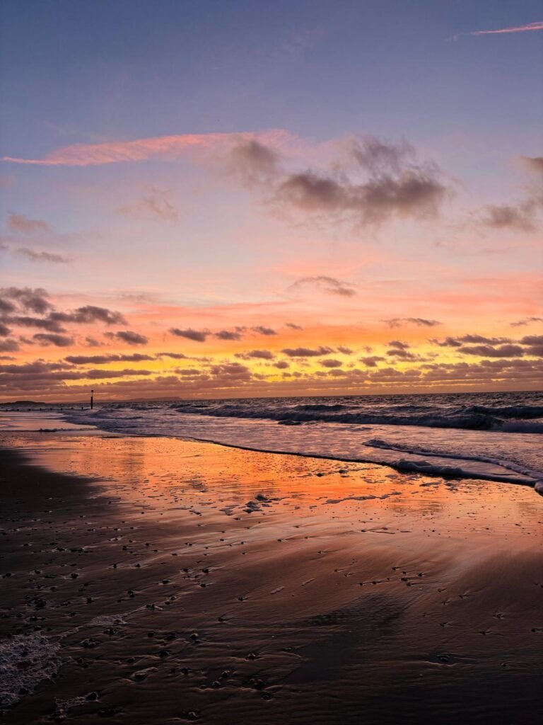 Dramatic sunrise over a Dorset beach with orange, red and purple sky reflected in wet sand as waves roll back into the sea