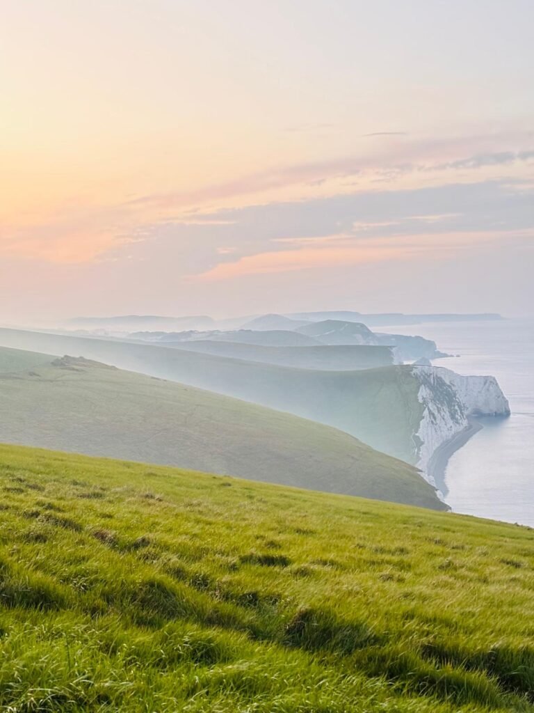 Dawn view east from White Nothe along grassy chalk cliffs toward Durdle Door with light ground mist
