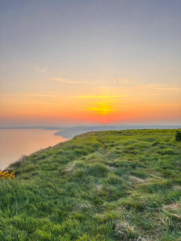 Small orange sun setting over the Dorset coast, viewed from a grassy hilltop with no visible trace of camping