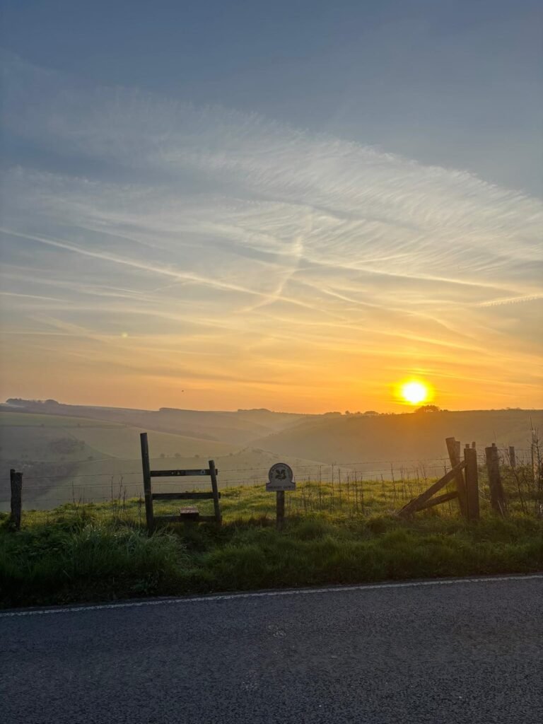 Misty sunrise over stile and National Trust sign at Melbury Down
