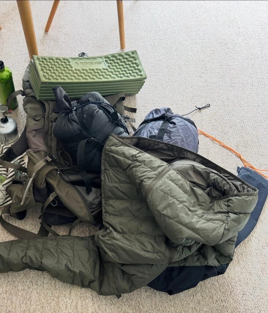 Basic beginner wild camping kit laid out on the floor with backpack sleeping bag and shelter