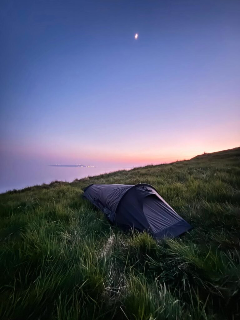 Nortent Skjul bivvi on a coastal cliff overlooking Portland at dusk