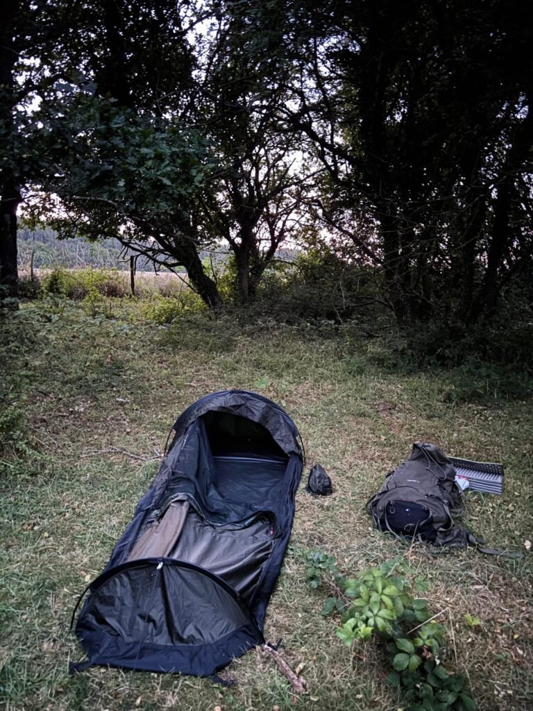 Nortent Skjul bivvi pitched in a woodland clearing with sleeping mat and backpack beside it.