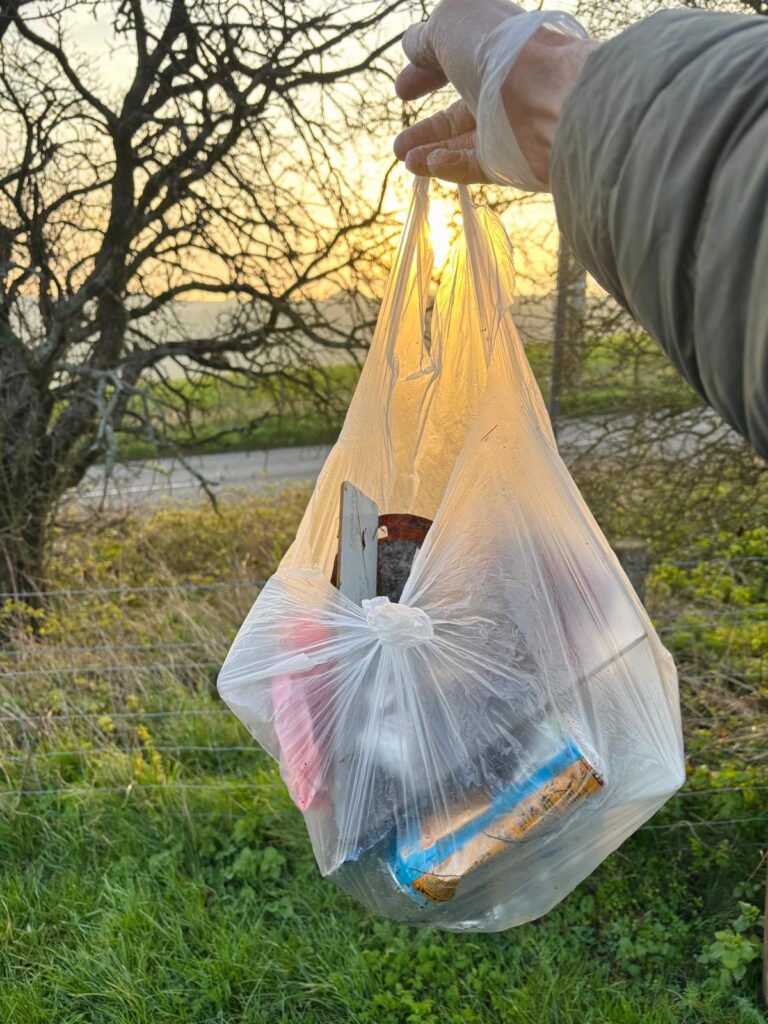 Full bag of litter held up after a litter pick with sunrise light shining through woodland trees.
