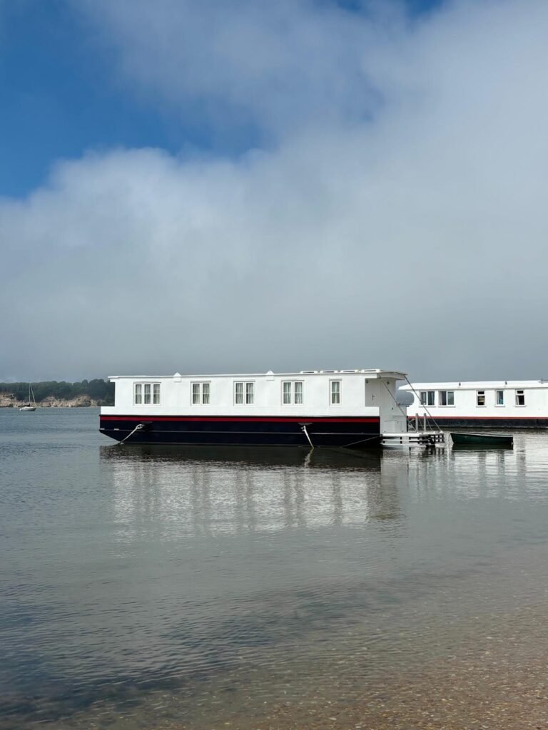 Two houseboats moored on the calm waters of Poole Harbour with Brownsea Island visible in the distance.