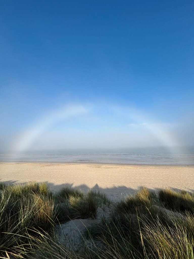 A fogbow visible above the sea beyond the beach and sand grass at Studland Bay.