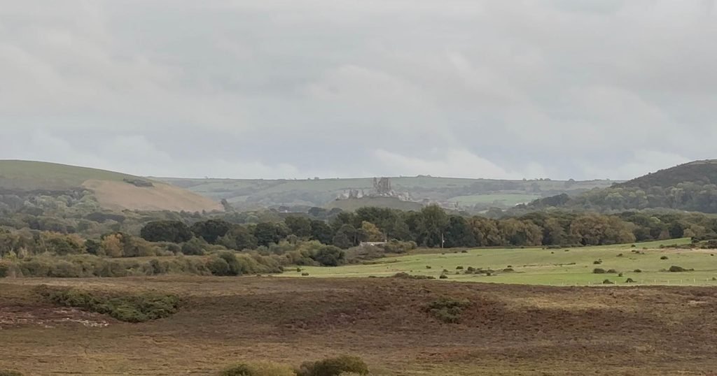 Corfe Castle on its hill between two larger hills in the Purbeck landscape